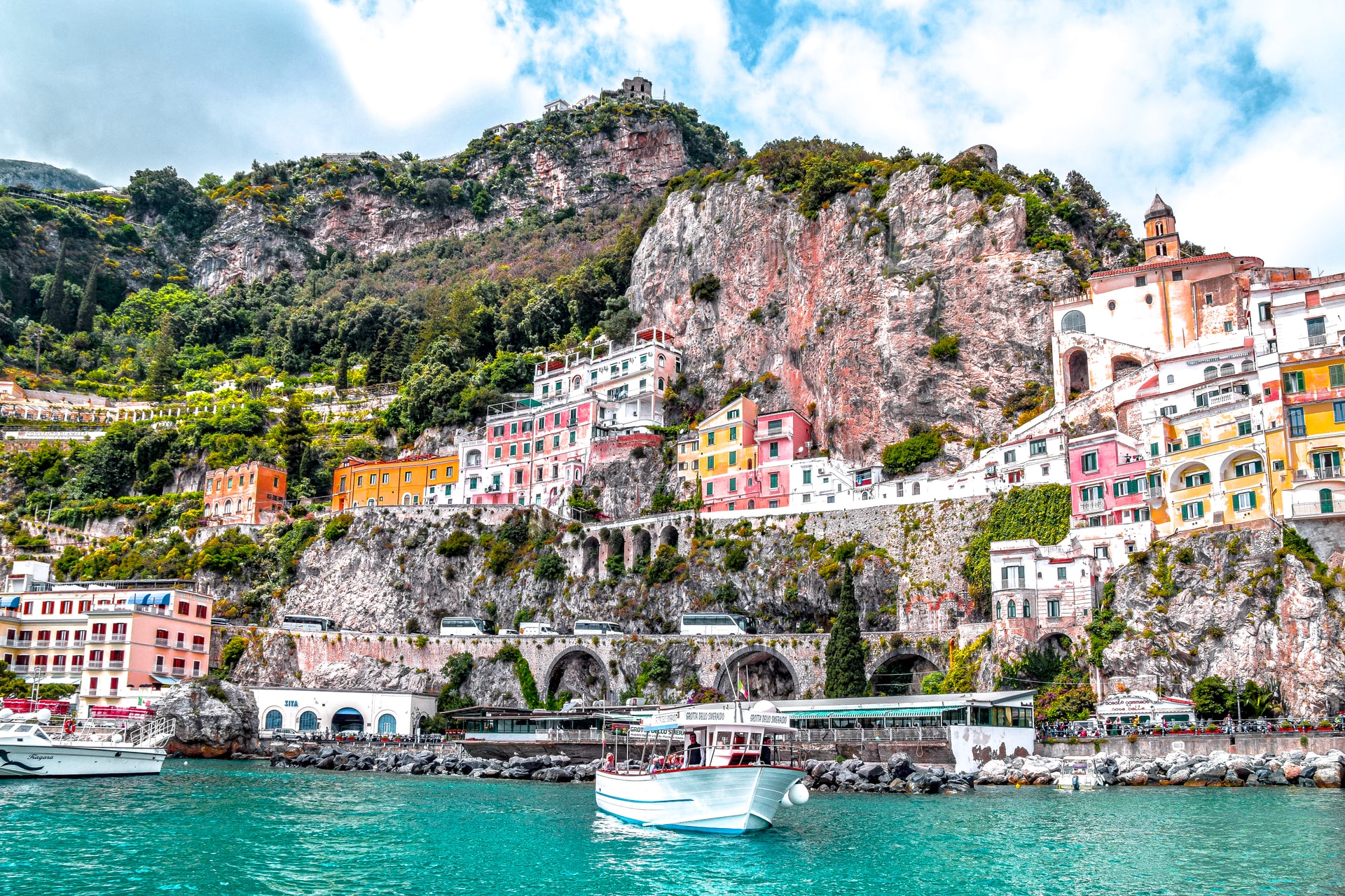 A view from the water of a town of colourful buildings are built along the steep incline of a cliff.
